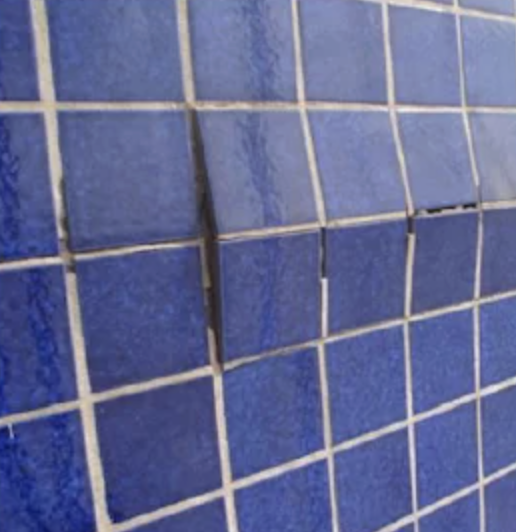 Pastilhas cerâmicas azuis de fachada desalinhadas e com juntas abertas, sinal de descolamento do revestimento