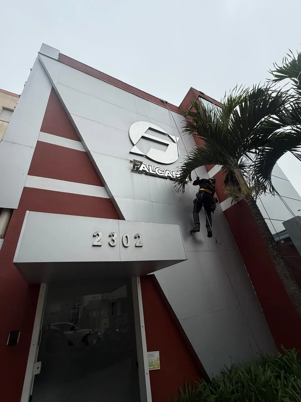Fachada da Falcare com técnico em acesso por corda limpando o ACM
