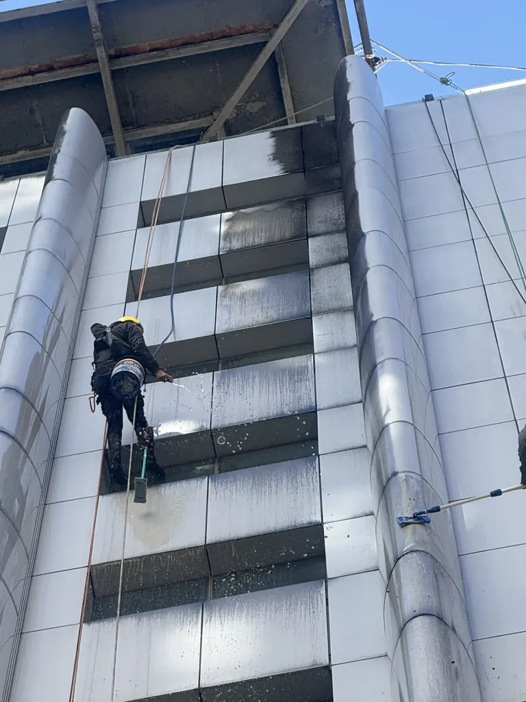 Técnico em corda lavando painéis de ACM do Hospital Paulistano, com a parte de cima ainda suja